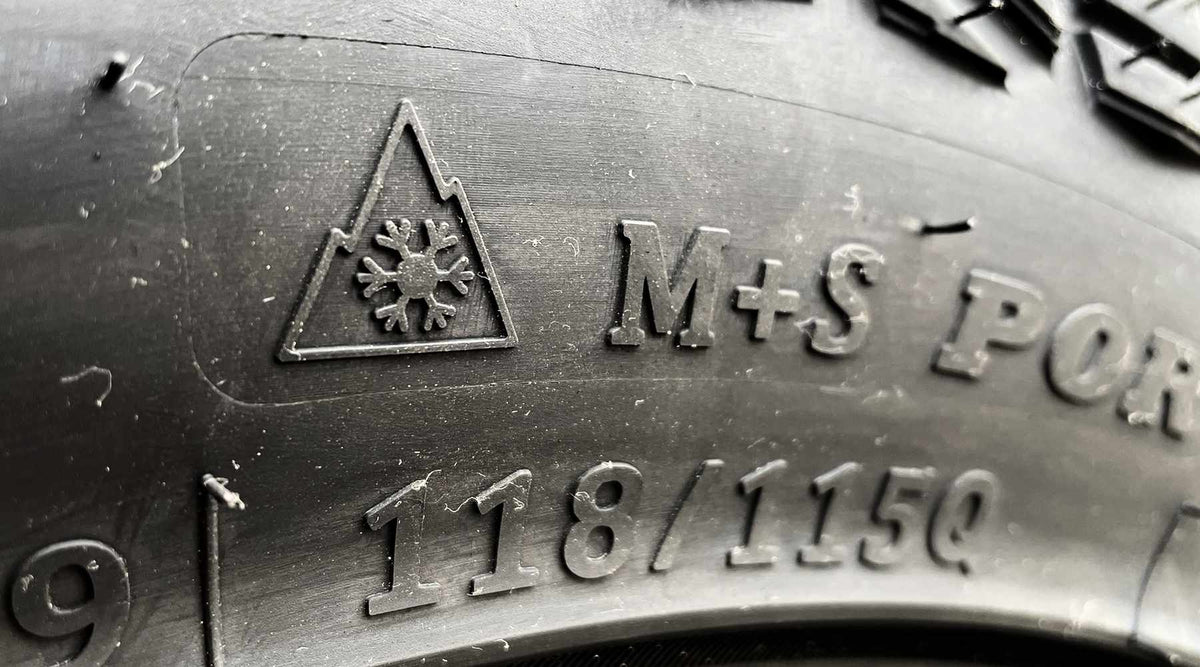 Close-up of a black rubber tyre sidewall showing embossed text and symbols, including 3PMSF, 'M+S POR' and the tread size '118/115Q'.