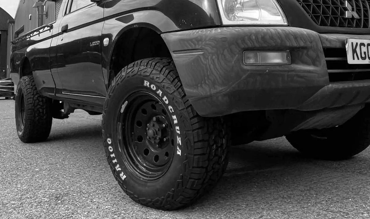 black mitsubishi l200 outside industrial unit with metal shutter. Fitted with all terrain tyres and wheels with roadcruza written on the sidewall