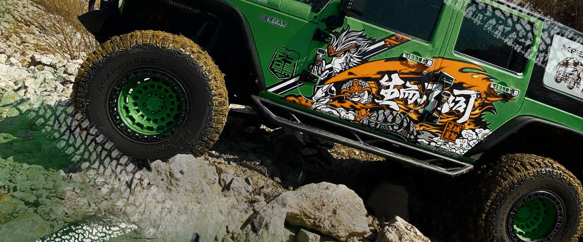 Green Jeep Wrangler with Chinese cartoon warrior graphic on the side, tackling some rocks with its huge 4x4 offroad tyres.